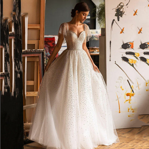 Robe de mariée élégante à paillettes, décolleté cœur, coupe trapèze, manches chauve-souris, dos nu en tulle.