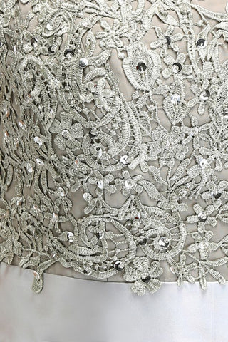 Robe de soirée argentée à manches courtes et décolleté trapèze, ornée d'appliques et d'une ceinture, longueur au sol.